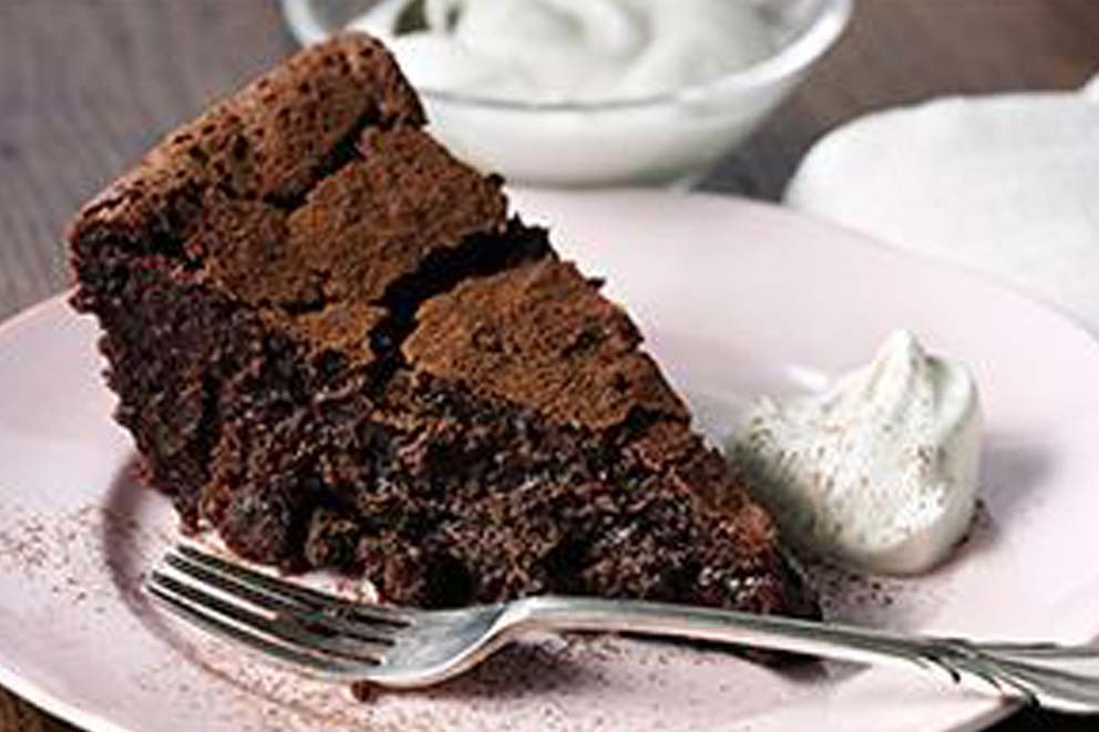 Raisin and bitter chocolate mud cake on a plate with cream on the side.