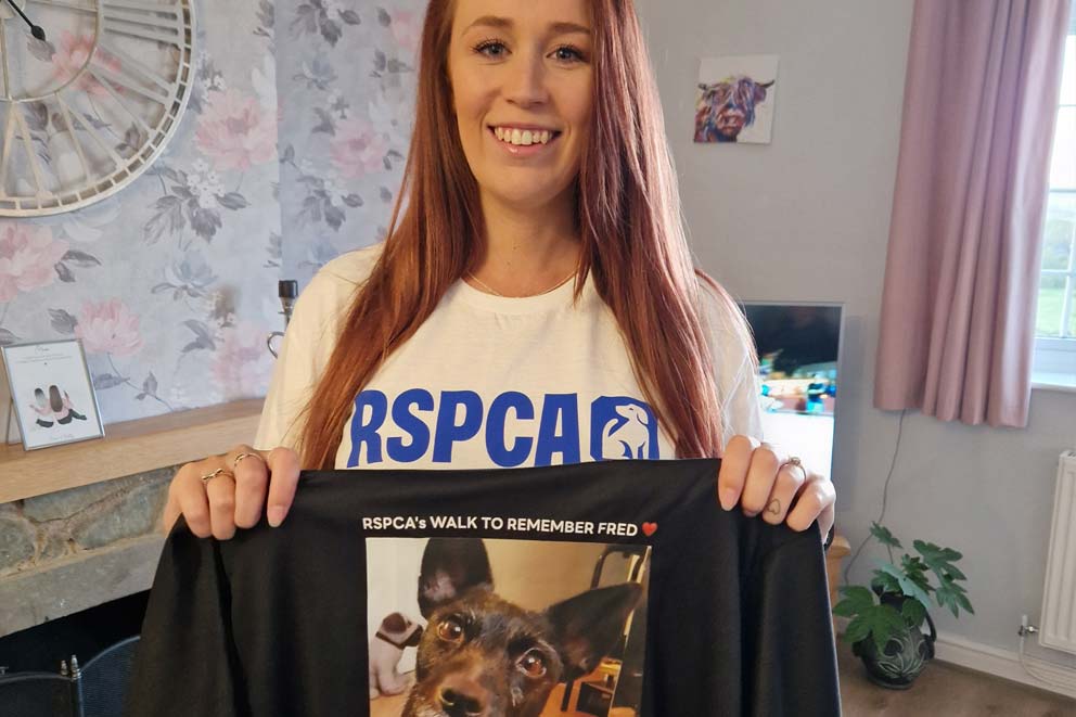 Holly Payne smiling and holding up a bespoke 'Walk to Remember Fred' t-shirt.