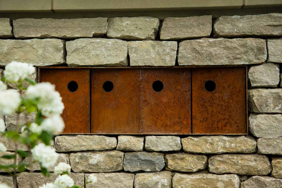 Four rusted metal-fronted bird boxes built into a stone wall, each with a round entrance hole.