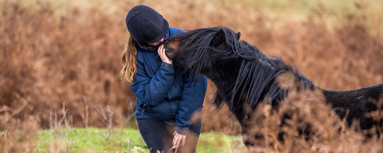 A small black and chestnut horse next to their owner who is wearing a riding hat.