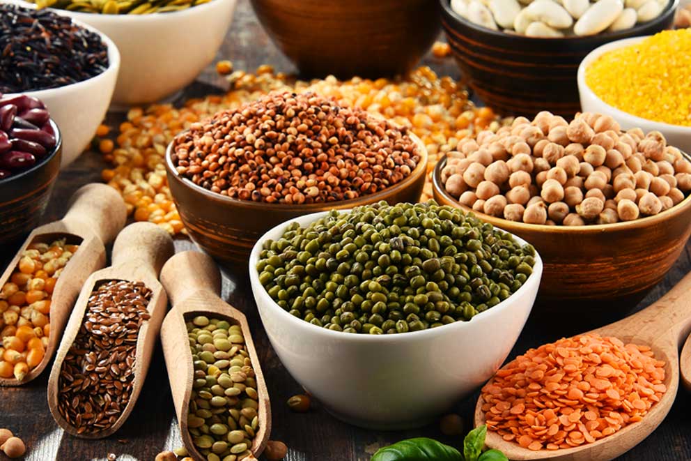A variety of dried beans, lentils and grains are displayed in rustic bowls and wooden scoops.