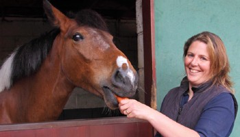 rehomed horse enjoying a carrot snack with smiling new owner