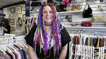 woman with colourful hair smiling as she stands inside a charity shop © RSPCA