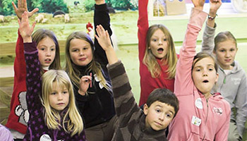 children in a classroom with raised hands